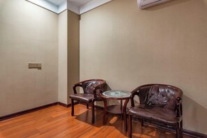 Une pièce avec un plancher en bois, deux fauteuils en cuir, une petite table en verre et un climatiseur fixé au mur.