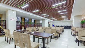 Un amplio comedor interior con varias mesas y sillas, techo de madera con plantas verdes y paneles decorativos en las paredes.
