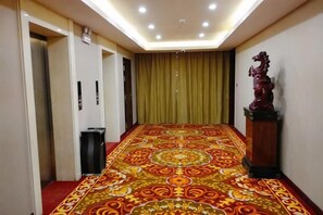 Un couloir d’hôtel avec un tapis à motifs, une poubelle, une statue et un rideau.