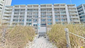 A multi-story hotel with a central entrance, surrounded by dry vegetation and a clear sky.