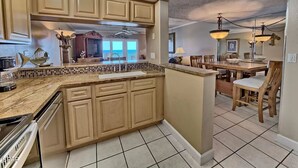 A kitchen with beige cabinets, a tiled backsplash, and a central island. There is a dining area with wooden chairs and a table.
