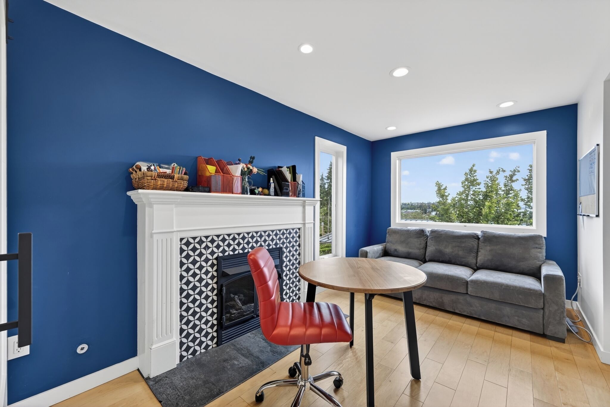 Une pièce avec un mur bleu, une cheminée, un canapé gris et une table ronde.
