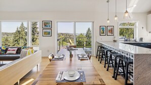 A modern kitchen with a long dining table, bar stools, and large windows offering a view of the outdoors. - 4-Bd w/ AC, Walk to Light Rail, Yard, VIEW Dog OK! (Seattle)