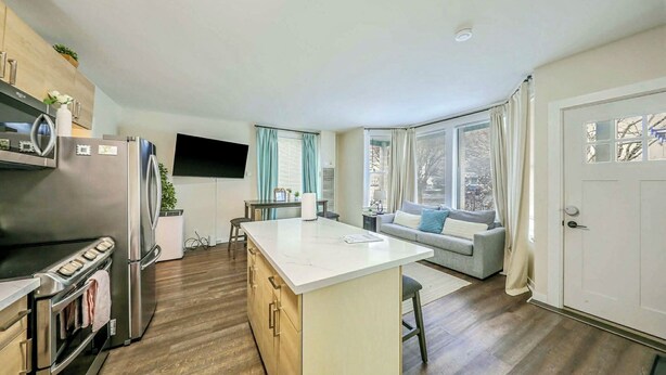 A modern kitchen with a central island, built-in appliances, and a seating area with a sofa and window views. - Stylish Deluxe Kitchen /King Bed/Laundry/Free Parking (Renton)