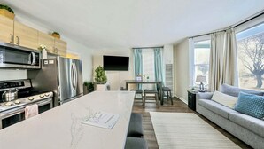 A modern kitchen with a central island, a dining area with a table and chairs, a sofa, and large windows with curtains. - Stylish Deluxe Kitchen /King Bed/Laundry/Free Parking (Renton)