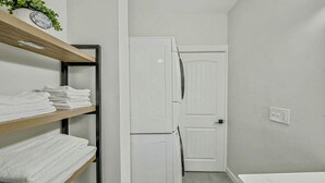A compact bathroom with a white sink, a white door, and a shelf with folded towels. - Stylish Deluxe Kitchen /King Bed/Laundry/Free Parking (Renton)
