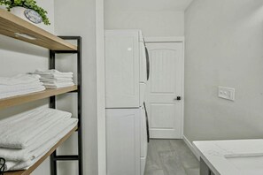 A compact bathroom with a white sink, a white door, and a shelf with folded towels. - Stylish Deluxe Kitchen /King Bed/Laundry/Free Parking (Renton)