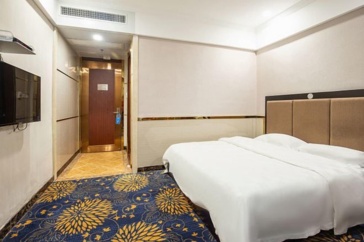 Ein Hotelzimmer mit einem Bett, einem Fernseher und einem gemusterten Teppich.