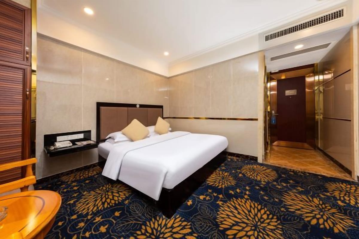 Une chambre d’hôtel avec un grand lit, une table de chevet, une chaise et une moquette à motifs.