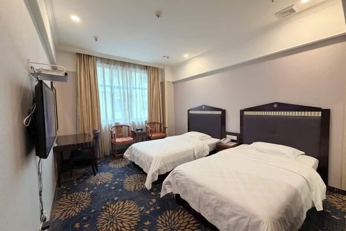 Hotelkamer met twee bedden, een bureau, een stoel, een televisie en een raam met gordijnen.