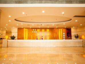 A hotel reception area with a reception desk, two staff members, and a decorative wall with framed items.