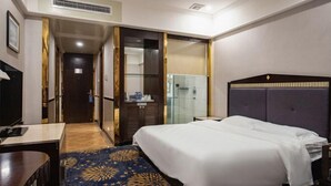 Une chambre d’hôtel avec un lit, un bureau, un miroir et une salle de bain visible à travers une porte ouverte.