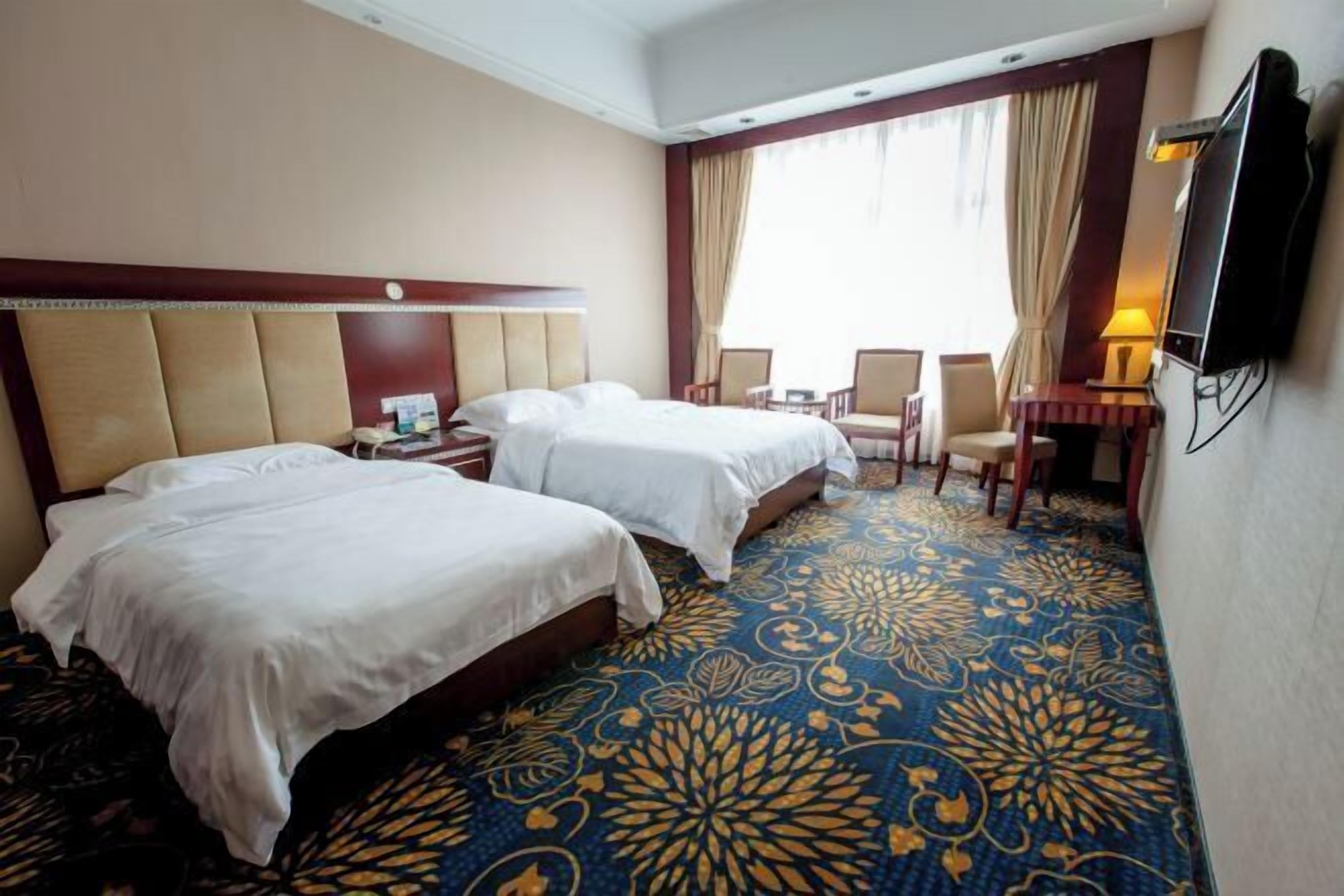 A hotel room with two beds, a desk, a chair, and a TV.