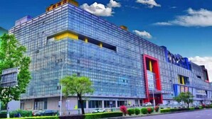 A modern building with a glass facade, multiple floors, and a prominent red and blue sign. - Huiquan Hotel (Zhongshan)