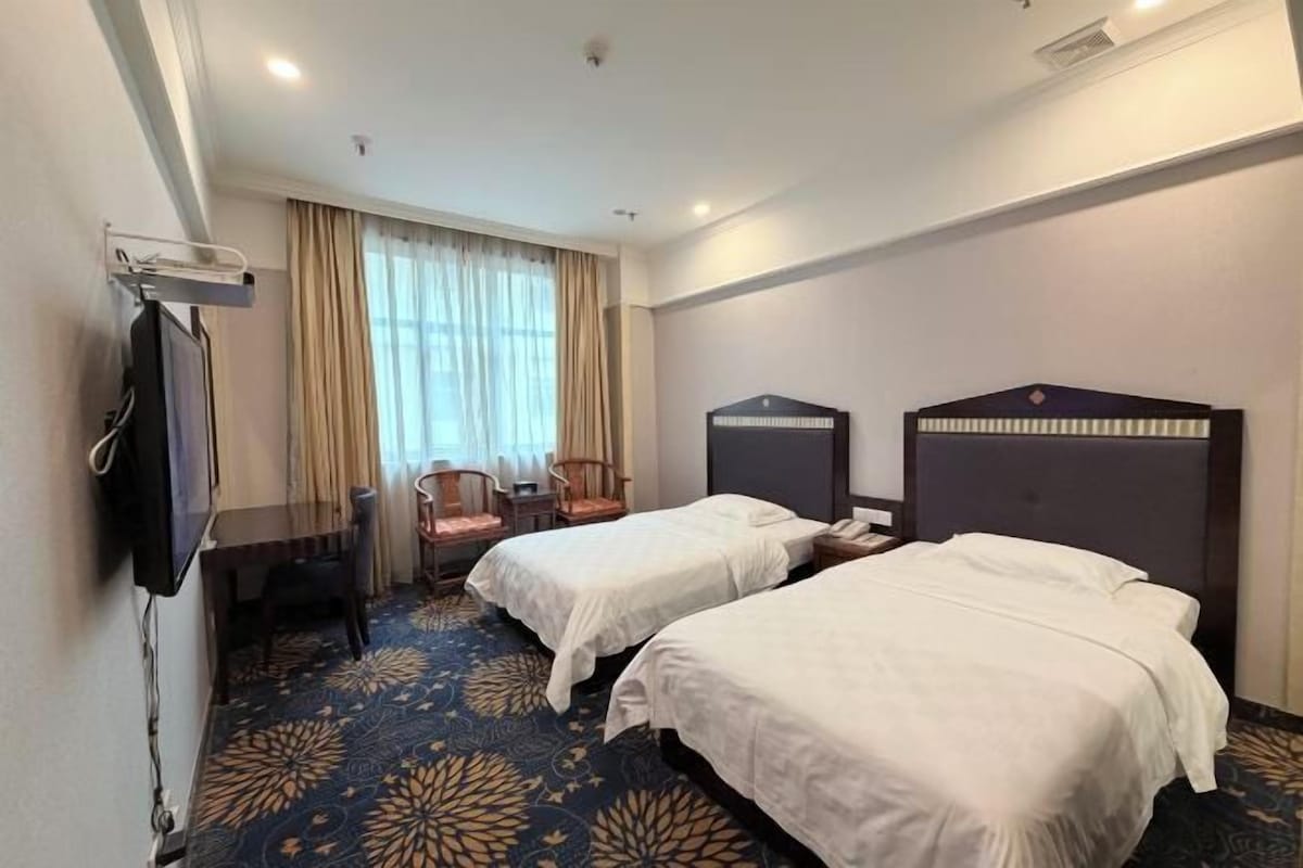 Une chambre d’hôtel avec deux lits, un bureau, une chaise, une télévision et une fenêtre avec des rideaux.