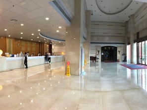 Um hall amplo com balcão de recepção, um pilar imponente e vista clara para a entrada.