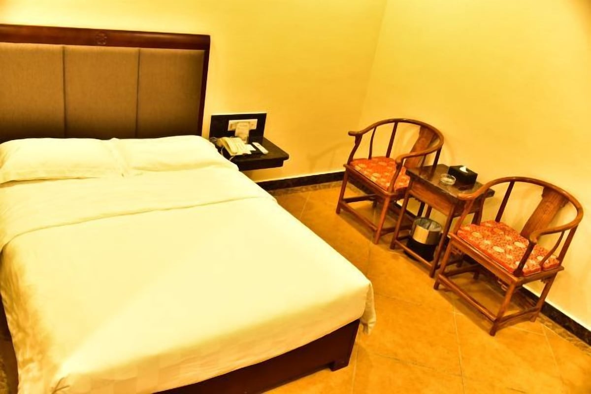 Une chambre d’hôtel comprenant un lit, une table de chevet, un téléphone et deux chaises en bois.