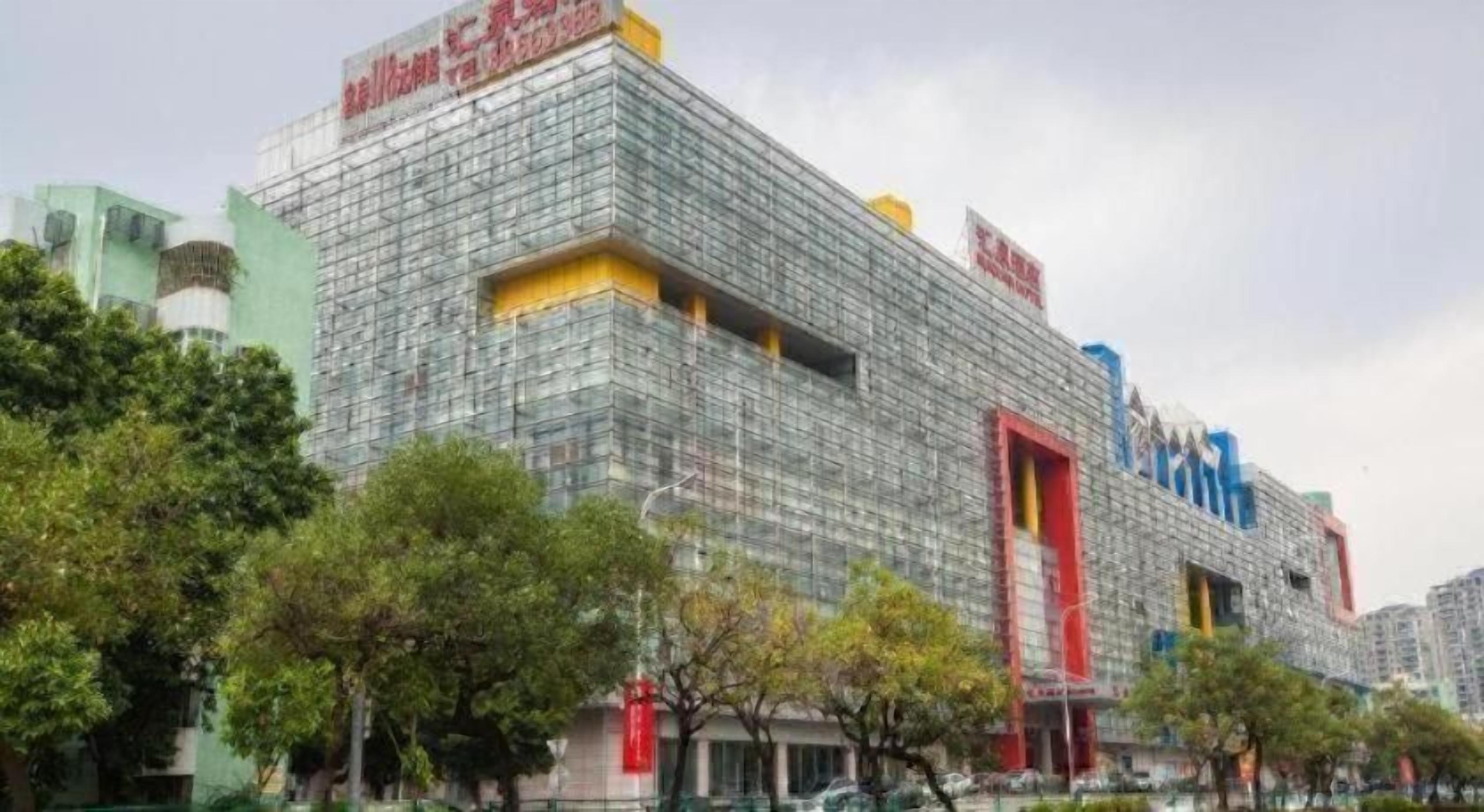 Un edificio moderno con fachada de vidrio, una entrada roja destacada y señalización que indica uso comercial.