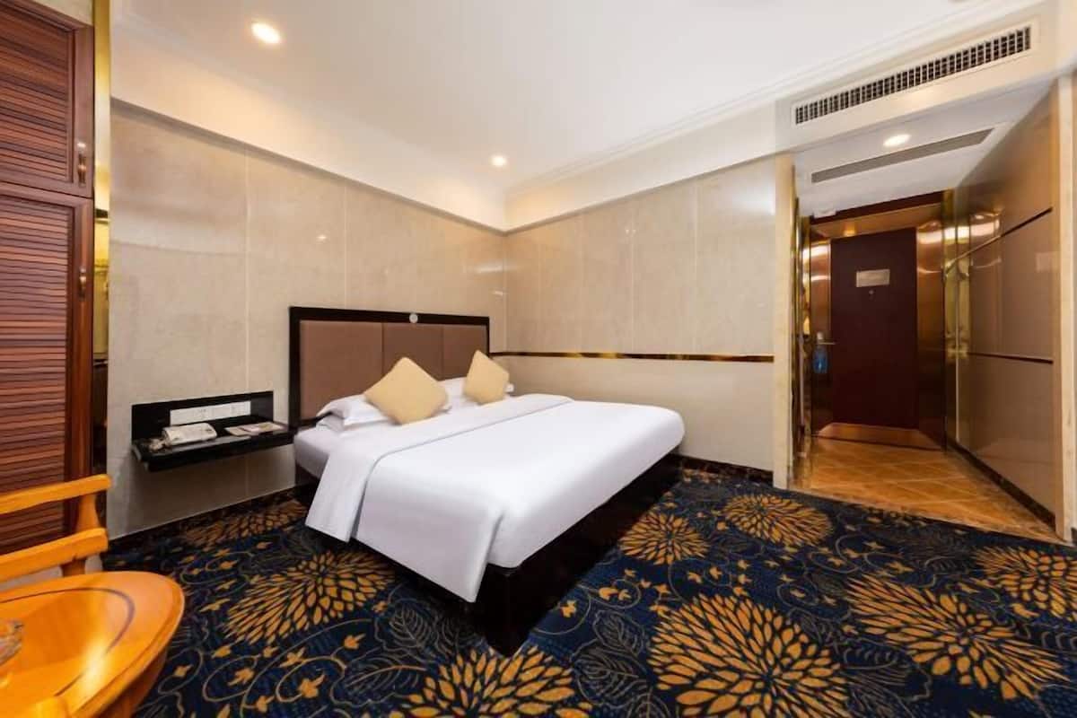 Een hotelkamer met een groot bed, een nachtkastje, een stoel en een kamerbreed tapijt met een patroon.