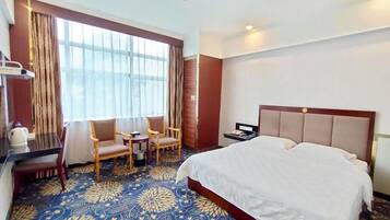 Una habitación de hotel con una cama grande, un escritorio con silla, una mesita y una ventana con cortinas.