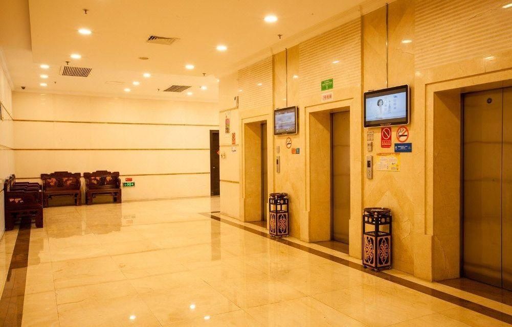Um saguão de hotel com piso lustroso, bancos de madeira e área de elevadores com visor digital.