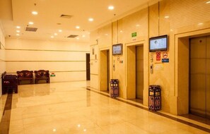 Recepció d'hotel amb un sòl polit, bancs de fusta i zona d'ascensor amb pantalla digital.