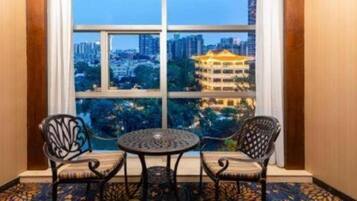 A room with two chairs and a table, a large window with a city view, and a patterned carpet.