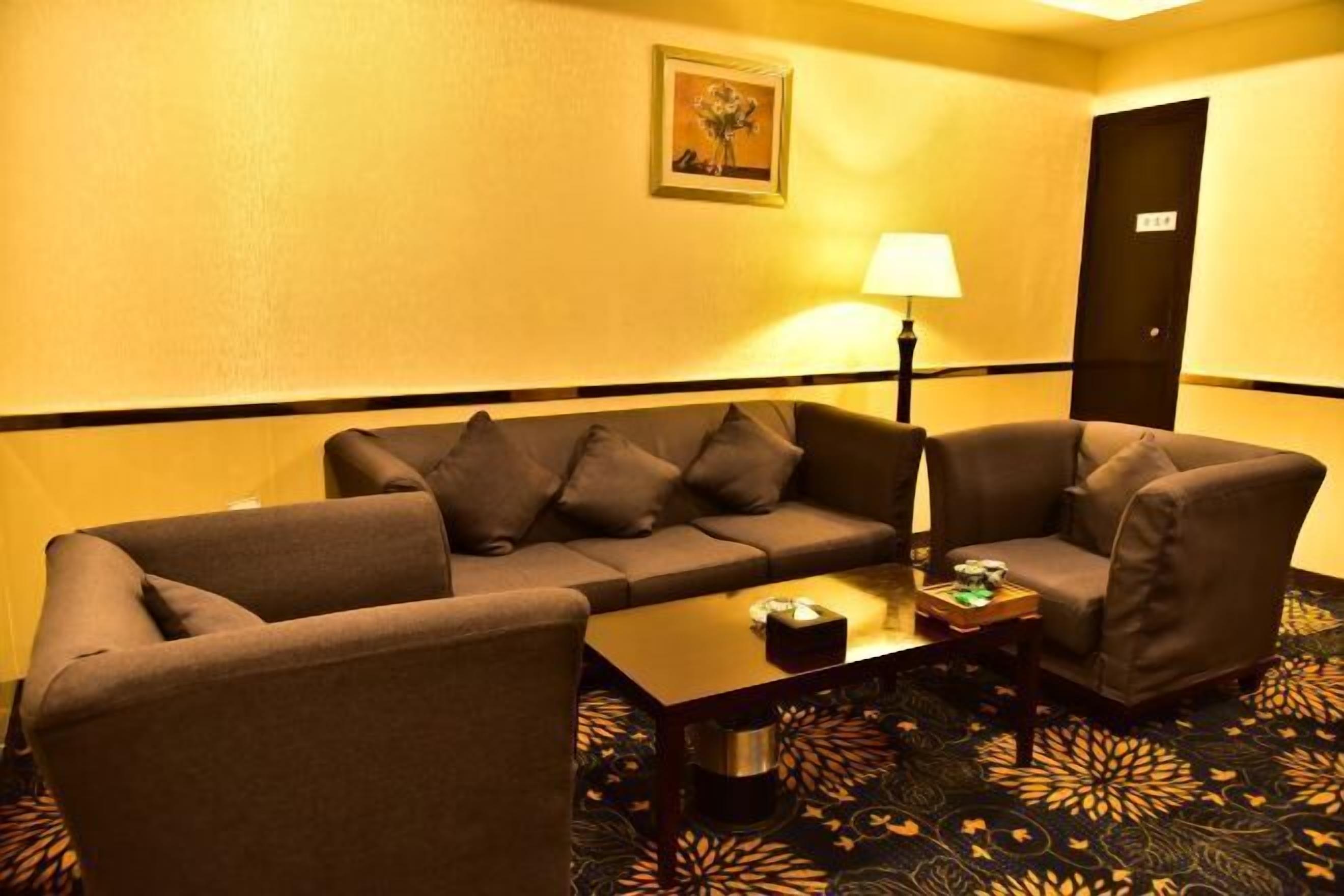 A hotel room with a sofa set, a coffee table, a lamp, and a patterned carpet.