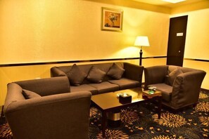 Ein Hotelzimmer mit einer Sofagarnitur, einem Couchtisch, einer Lampe und einem gemusterten Teppich.
