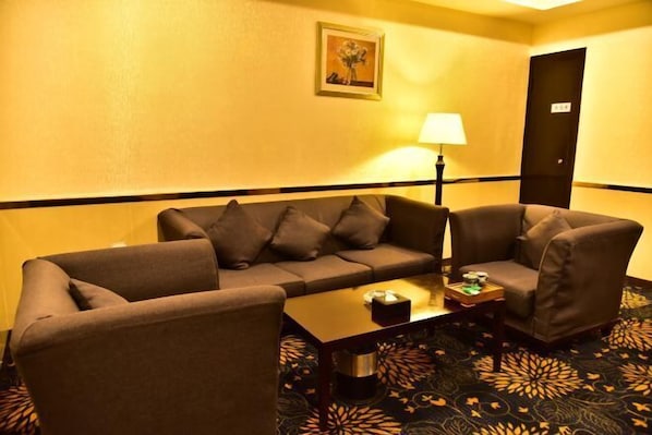 A hotel room with a sofa set, a coffee table, a lamp, and a patterned carpet. - Huiquan Hotel (Zhongshan)