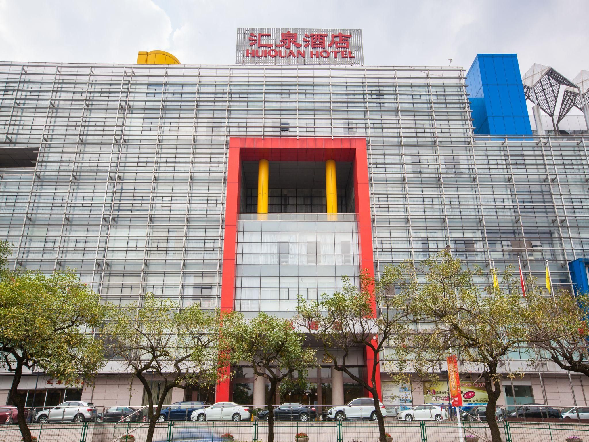 A modern hotel building with a prominent red and yellow entrance, multiple windows, and a blue structural element on the right.