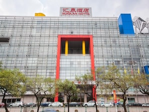 Um hotel moderno com fachada destacada em vermelho e amarelo, diversas janelas e um elemento estrutural azul à direita.