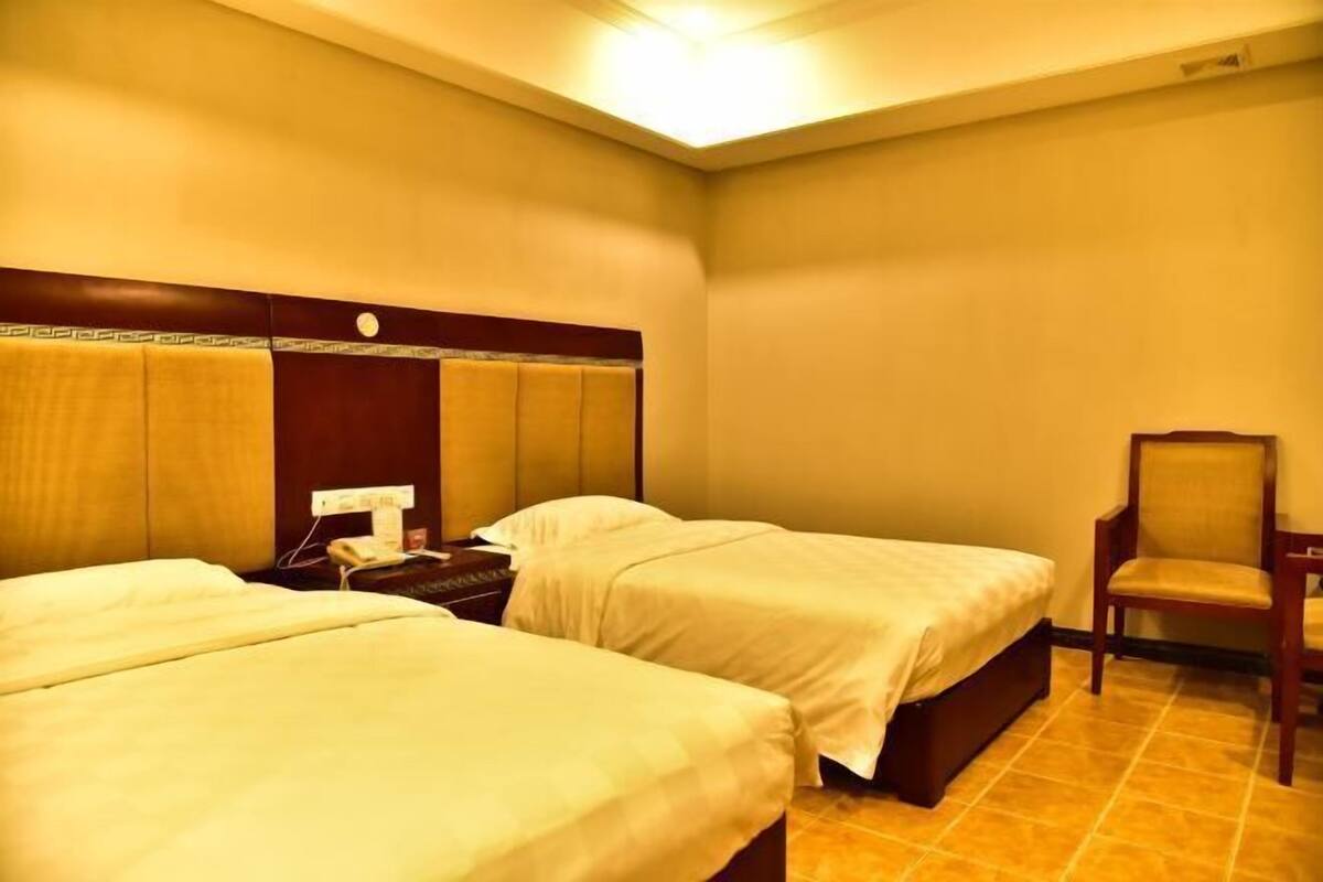 Een hotelkamer met twee bedden, een nachtkastje, een stoel en een aan de muur bevestigde telefoon.