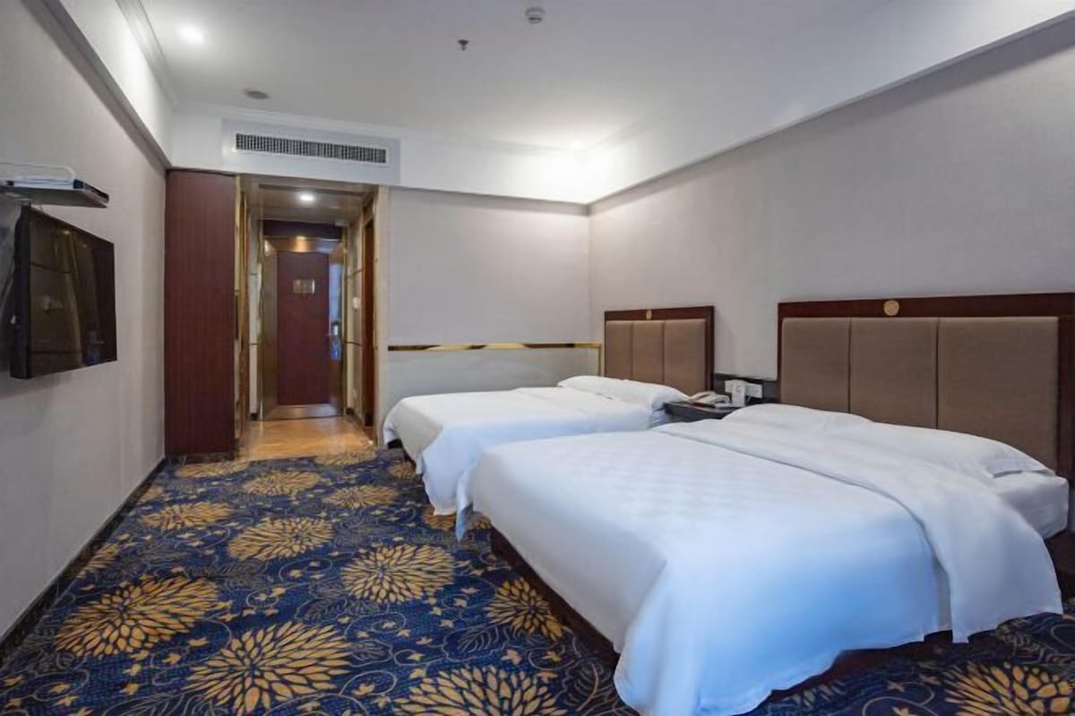Une chambre d’hôtel avec deux lits, une moquette à motifs, une tête de lit en bois et une porte donnant sur une autre pièce.