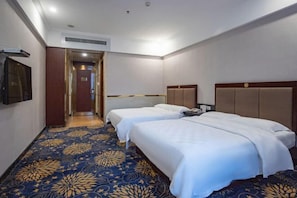 A hotel room with two beds, a patterned carpet, a wooden headboard, and a door leading to another room. - Huiquan Hotel (Zhongshan)