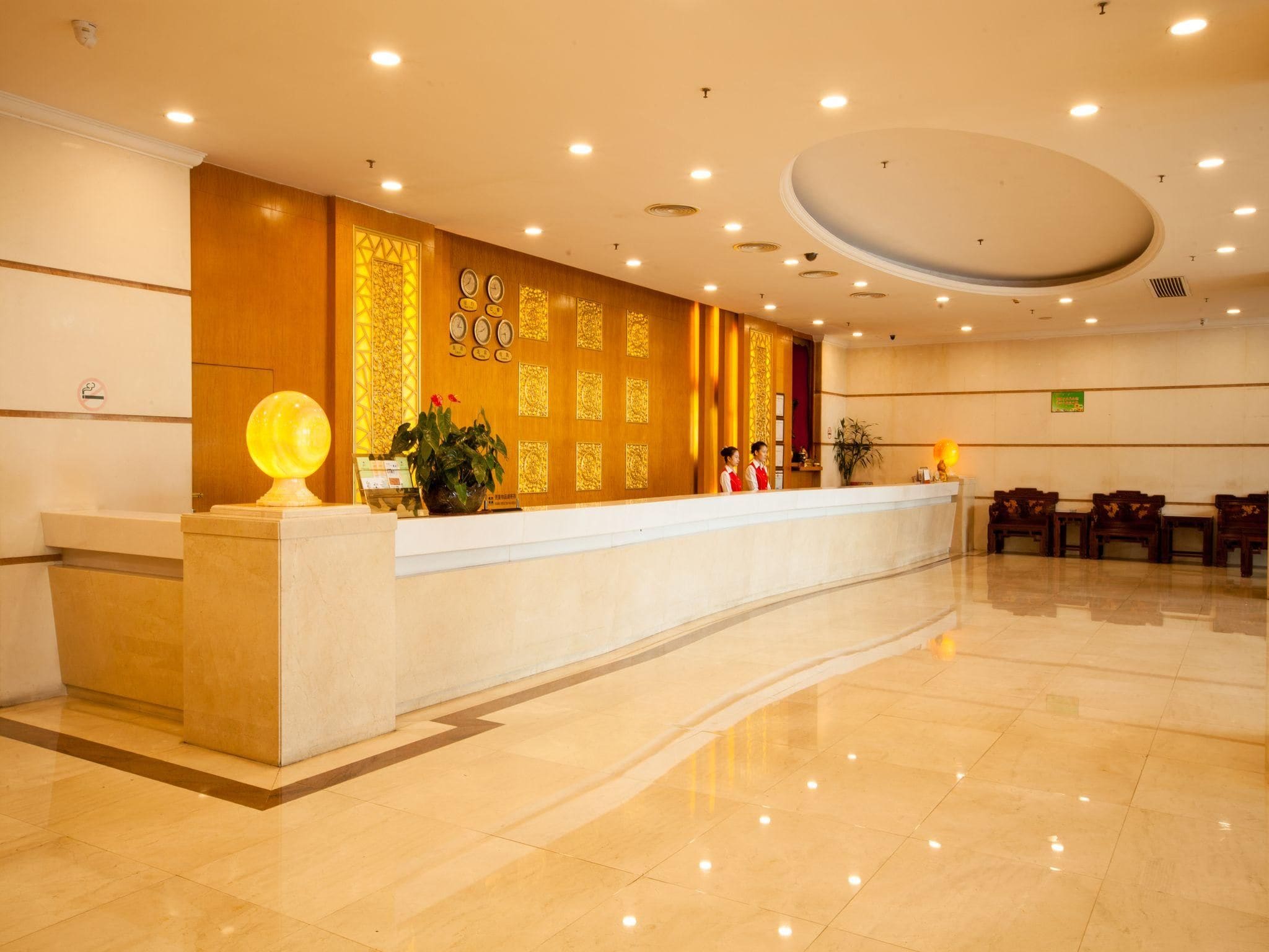 Uma área de recepção de hotel com piso de mármore, balcão de recepção e uma parede com relógios e painéis decorativos.