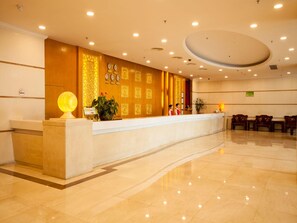 Un hall d’hôtel doté d’un sol en marbre, d’un comptoir d’accueil et d’un mur orné d’horloges et de panneaux décoratifs.