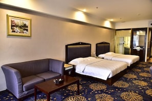 A hotel room with a sofa, two beds, a small table, and a patterned carpet. - Huiquan Hotel (Zhongshan)