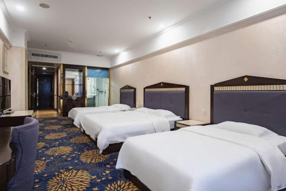 Een hotelkamer met drie bedden, een bureau en een kamerbreed tapijt met dessin.