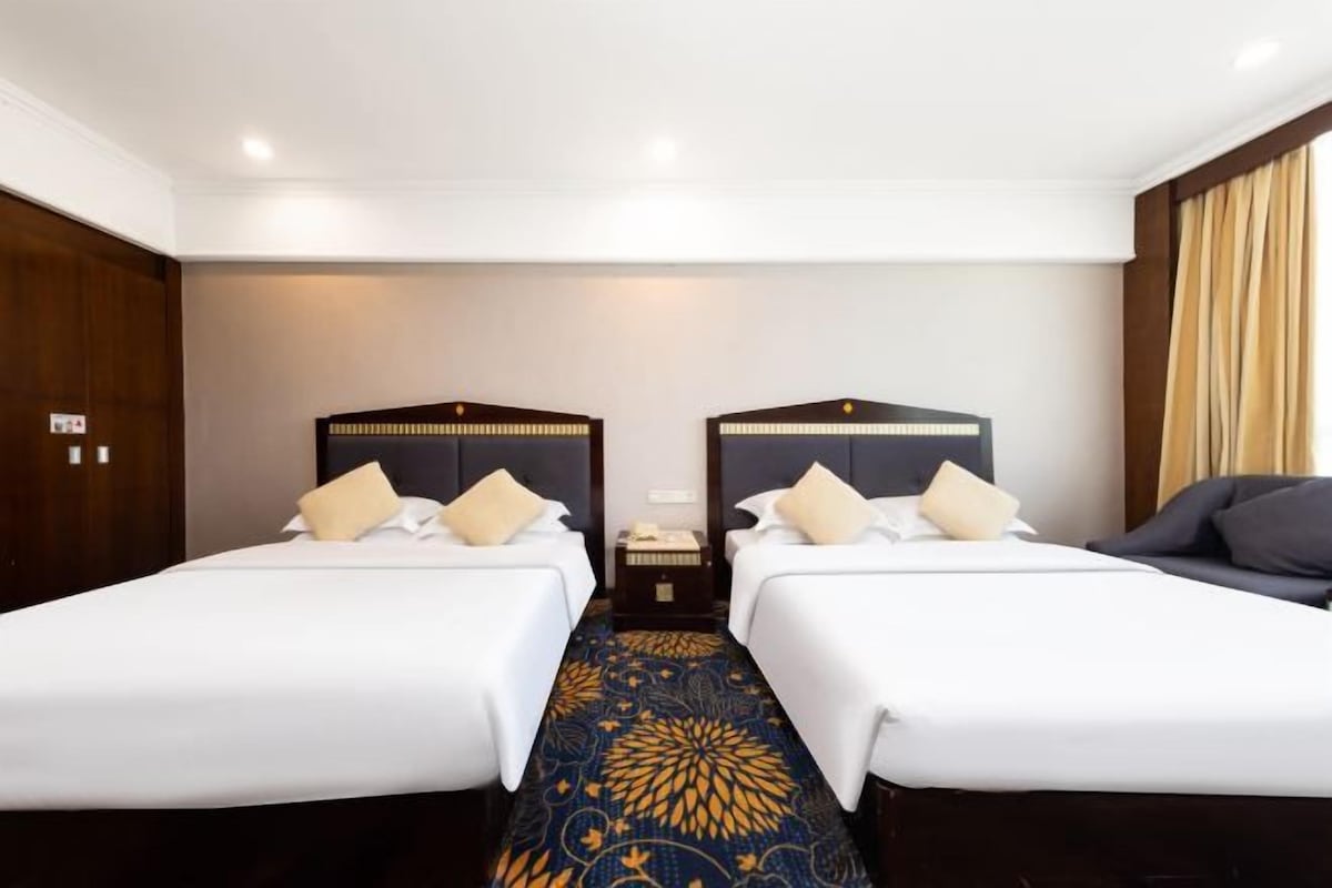 Une chambre d’hôtel avec deux lits simples, un canapé, une table de chevet et une moquette à motifs.