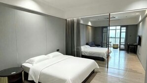 A hotel room with two beds, a round table, a TV, and a view of the city. - Huiquan Hotel (Zhongshan)