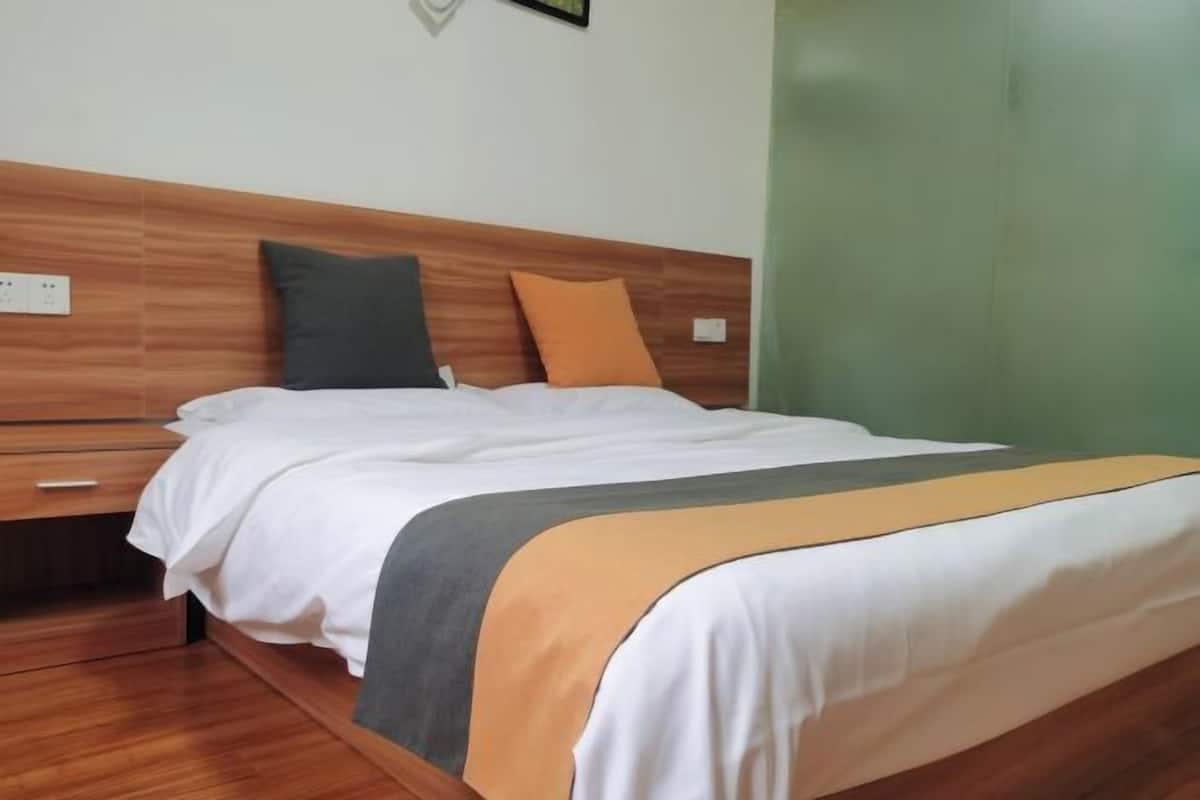 A neatly made bed with a wooden headboard, a bedside table, and a green wall.