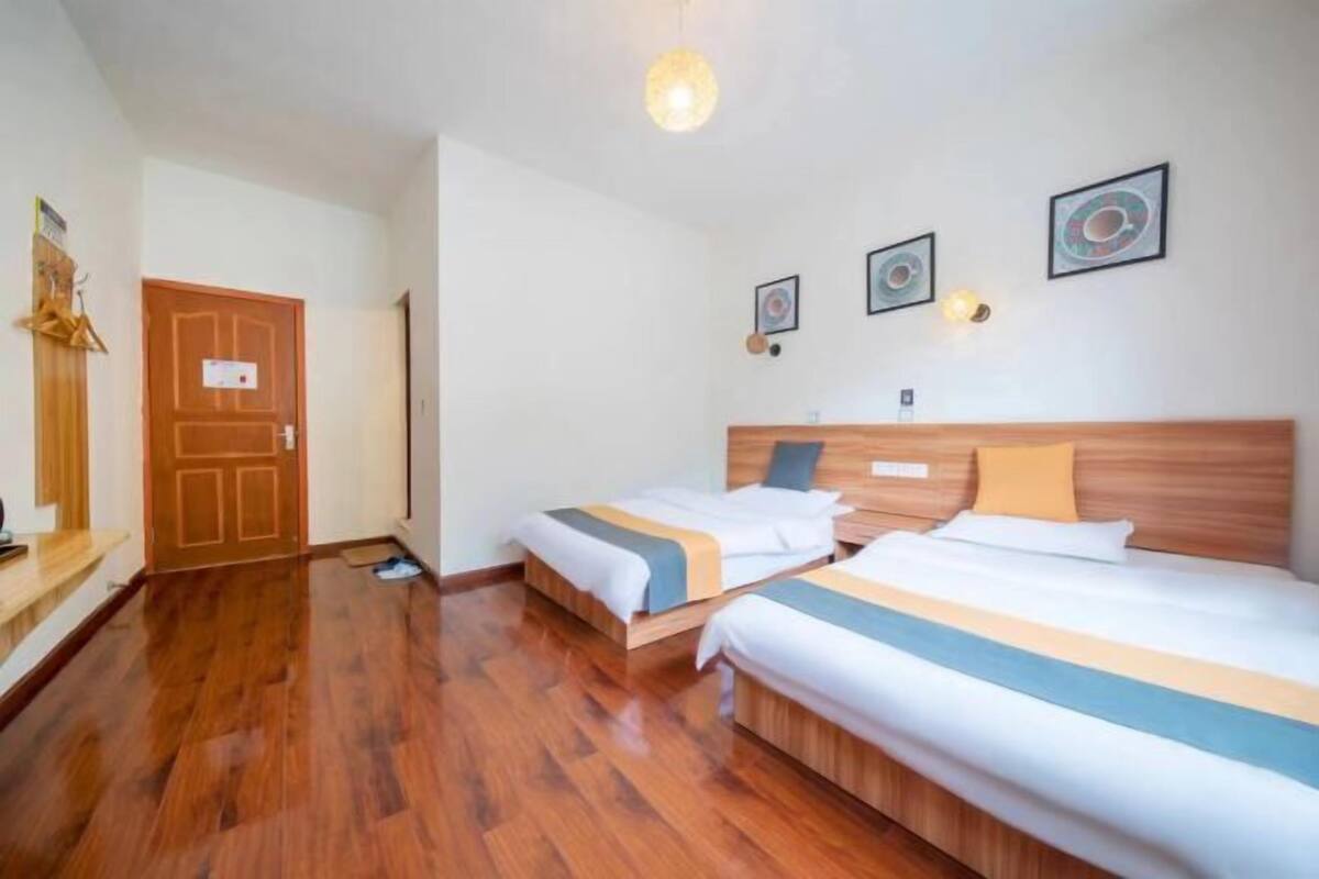 A hotel room with two beds, wooden flooring, a wooden headboard, and wall-mounted artwork.