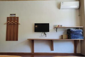 A room with a mounted TV, a wooden shelf with folded clothes, a wall-mounted air conditioner, and a wooden coat rack with hangers. - Miyi lnn (Xiaojin)