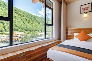 A hotel room with a large window, wooden bench, bed with pillows, and a framed picture on the wall. - Miyi lnn (Xiaojin)