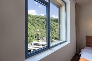 A hotel room with a large window, a bed, and a view of a forested area. - Miyi lnn (Xiaojin)