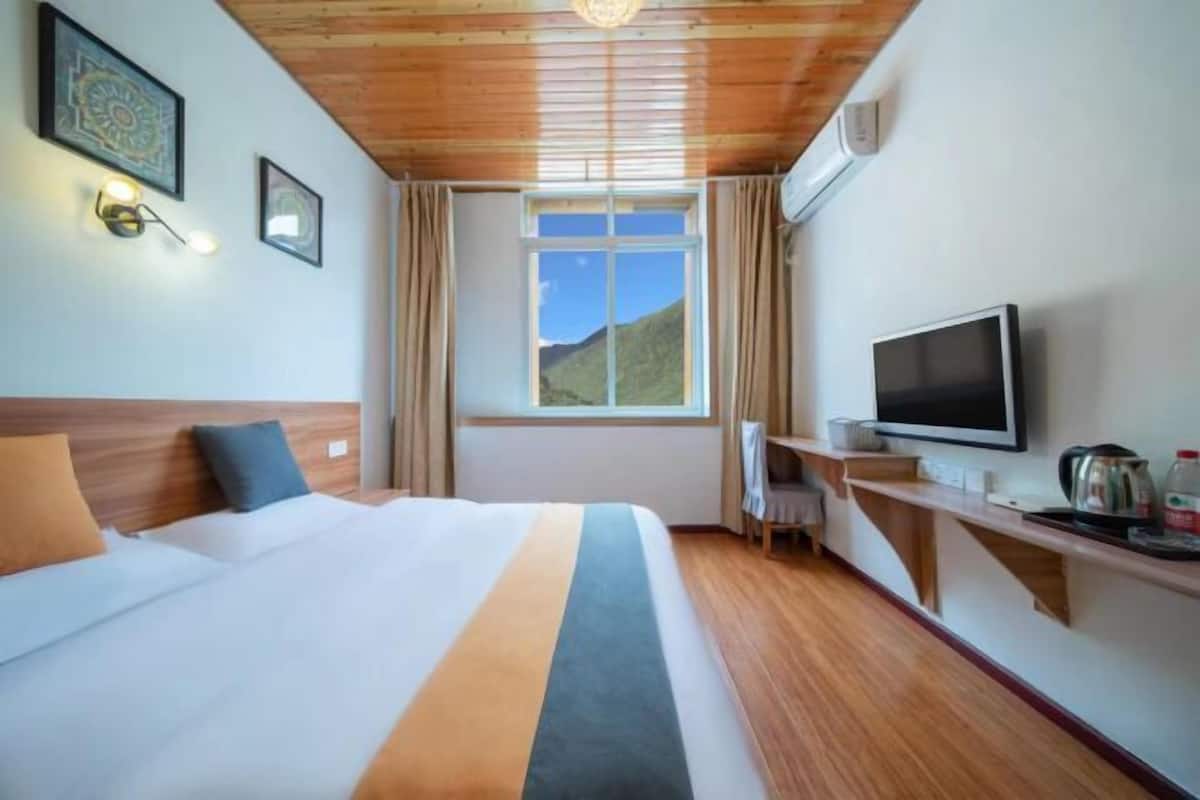A hotel room with a bed, a television, a desk, and a window with a view of the outdoors.