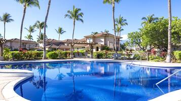 A swimming pool surrounded by palm trees and a building with a tiled roof.