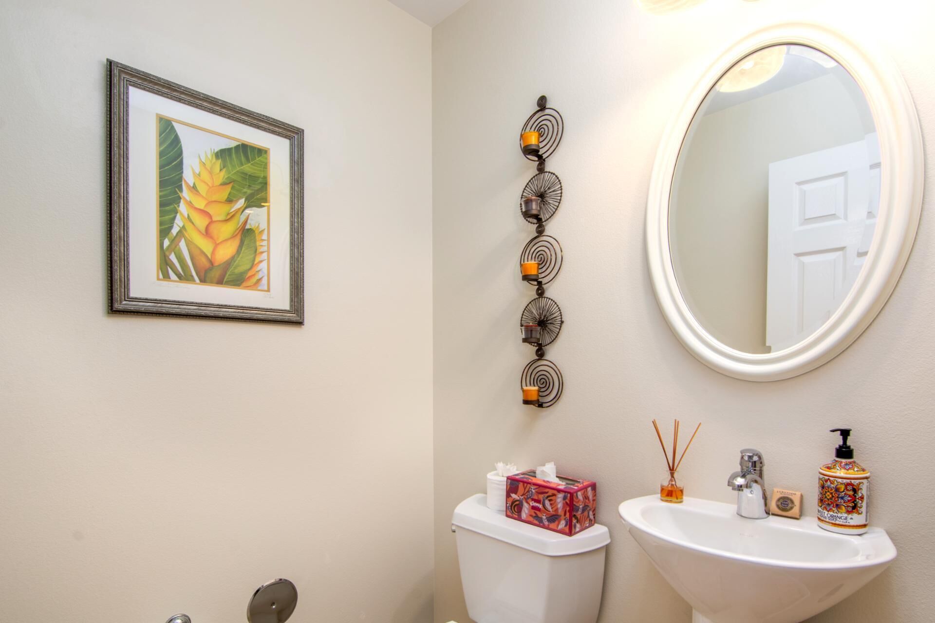 A bathroom with a toilet, sink, framed artwork, decorative wall piece, and a mirror.