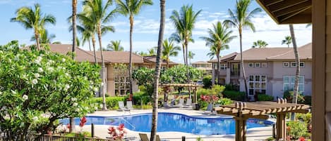 A pool area with lounge chairs, palm trees, and a building with a tiled roof.